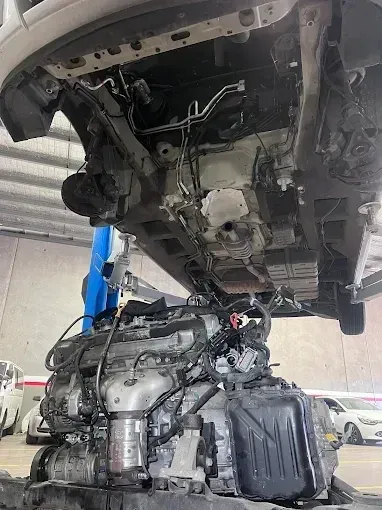 Engine being removed from underneath a vehicle raised on a hoist