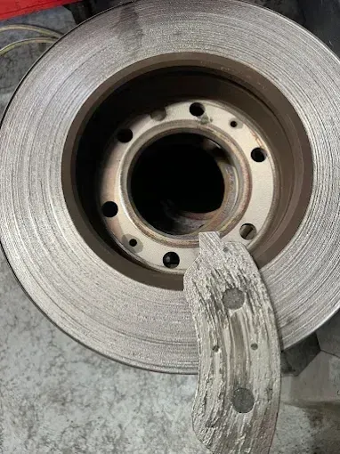 Worn brake disc and brake pad removed from a car during a brake repair